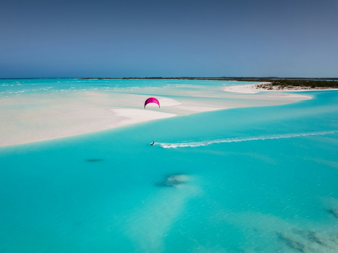 A pale sandbar curving through the bright turquoise shallows of the Exumas.