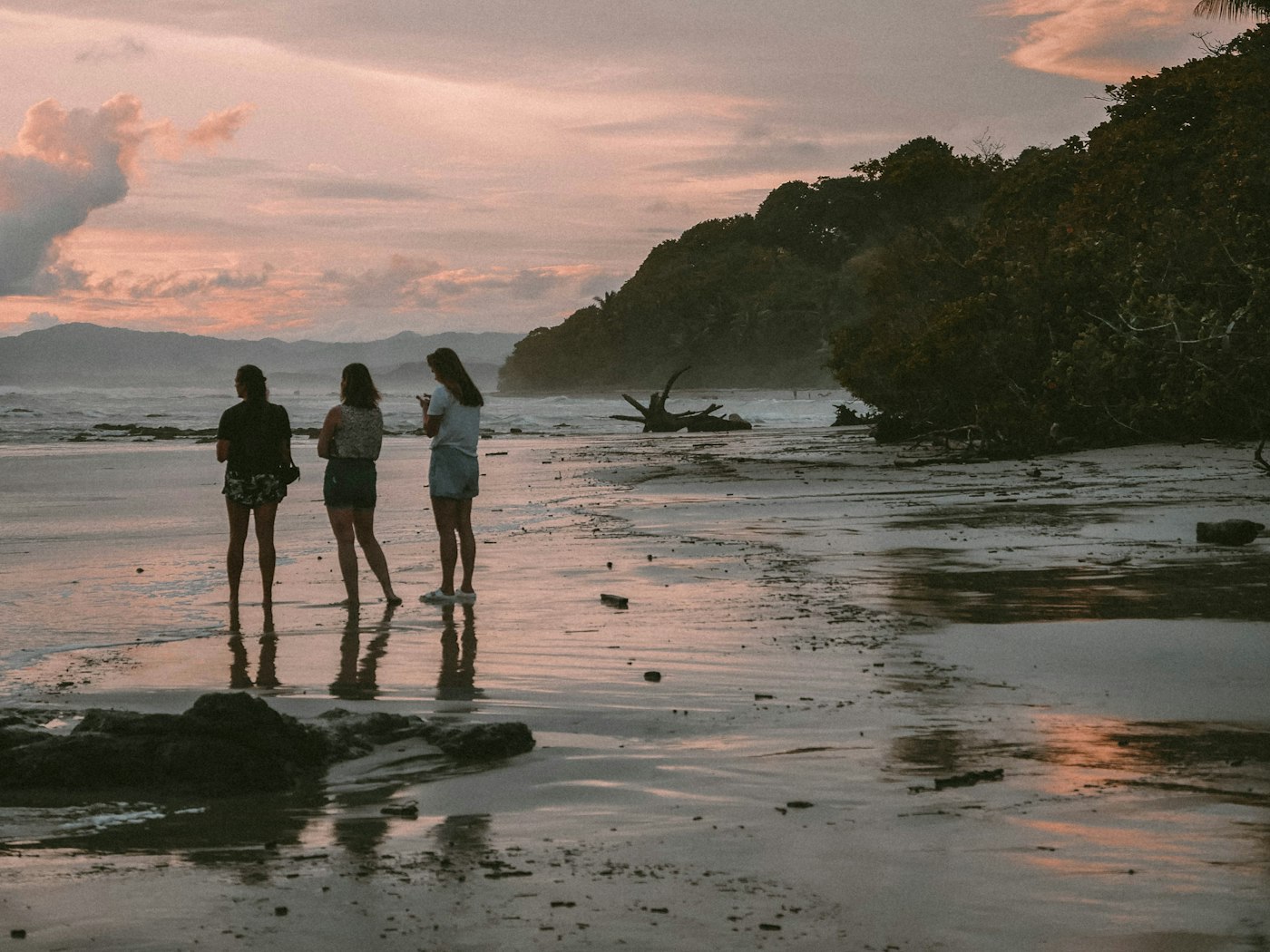 Three people on a wide Pacific beach in Costa Rica as the sky turns pink at dusk.