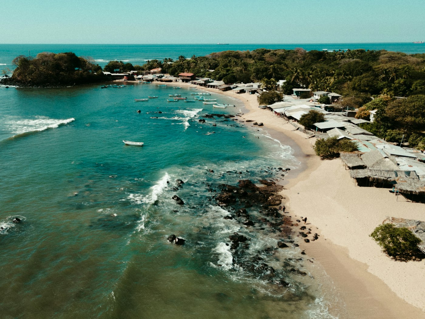An aerial view of a Salvadoran fishing village along a curved bay with boats moored offshore.