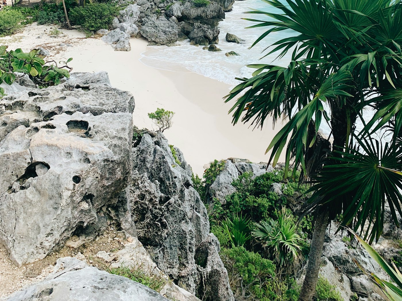A small white-sand cove below limestone rocks and palms on the Caribbean coast of Mexico.