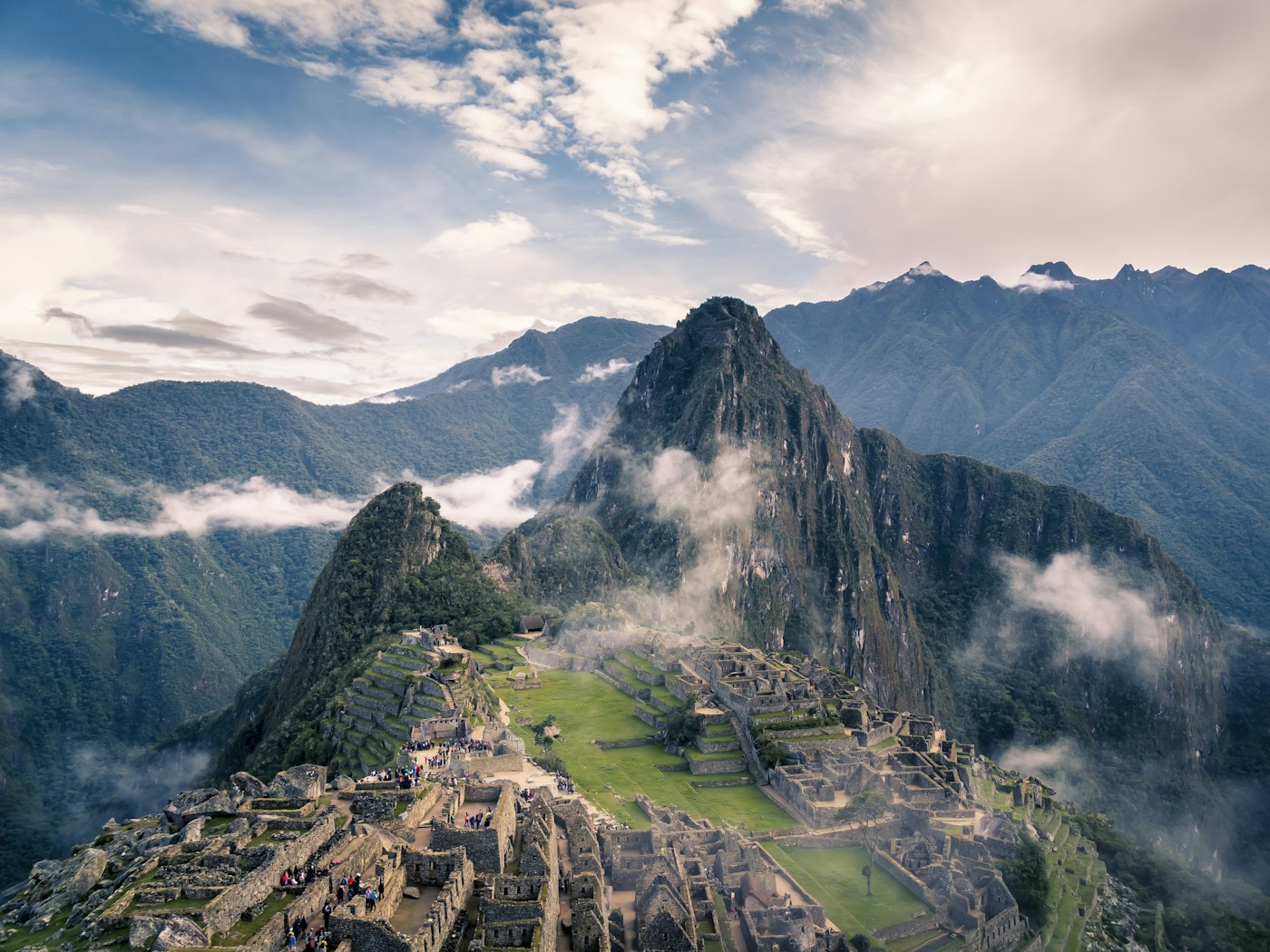 Machu Picchu's terraces on the ridge, cloud drifting across the peaks behind.