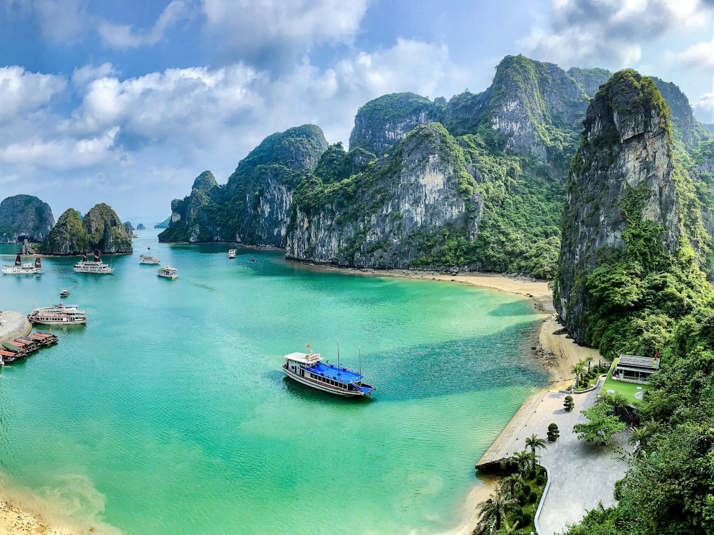 Limestone karsts rising from the jade water of Ha Long Bay, junk boats moored below.
